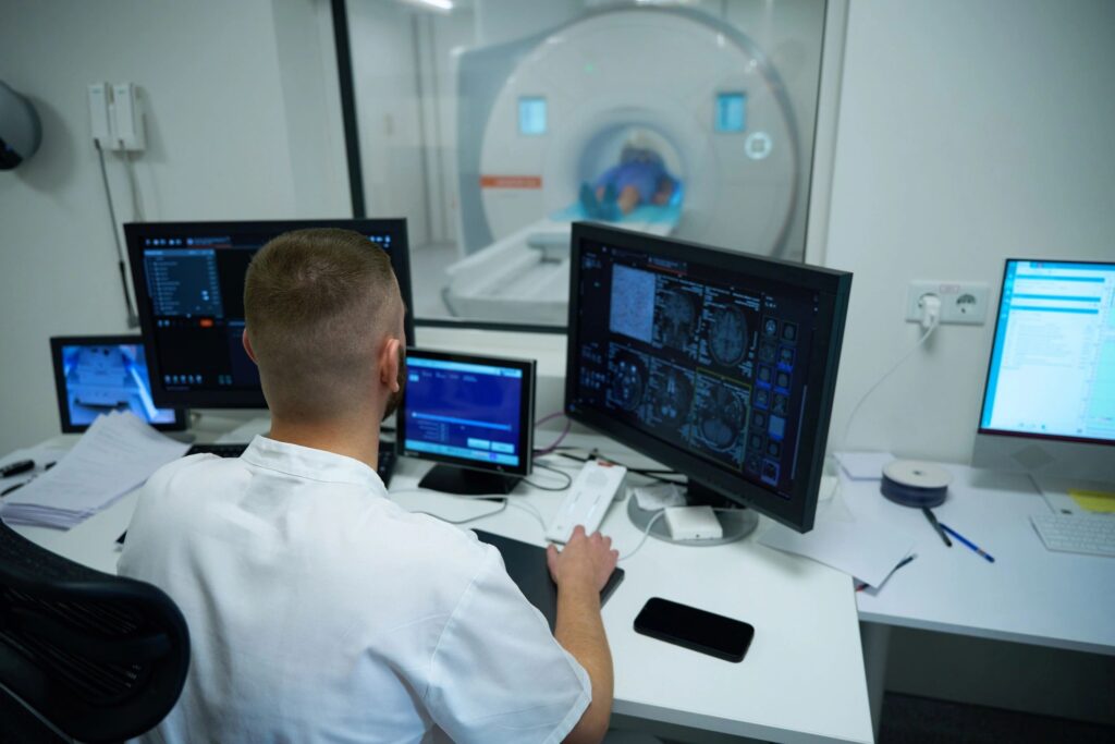 Premier Diagnostics technician seated at desk in control room viewing head MRI scans on computer monitor.